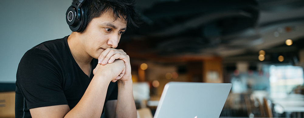 A man wearing headphones looks intensely at his laptop.