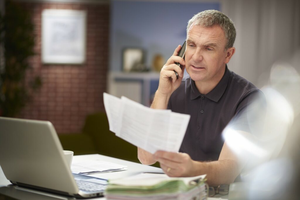 A business owner talks on the phone while reviewing paperwork.